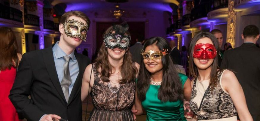 Four med students are dressed in formal attire and wearing eye masks