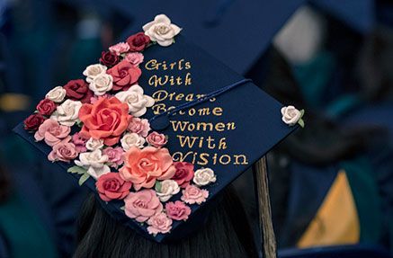 A graduation cap adorned with flowers reading "Girls with dreams become women with vision"