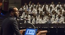 A man speaks at a podium to a crowd of med students