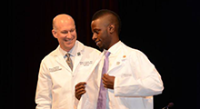Faculty member putting a white coat on a student
