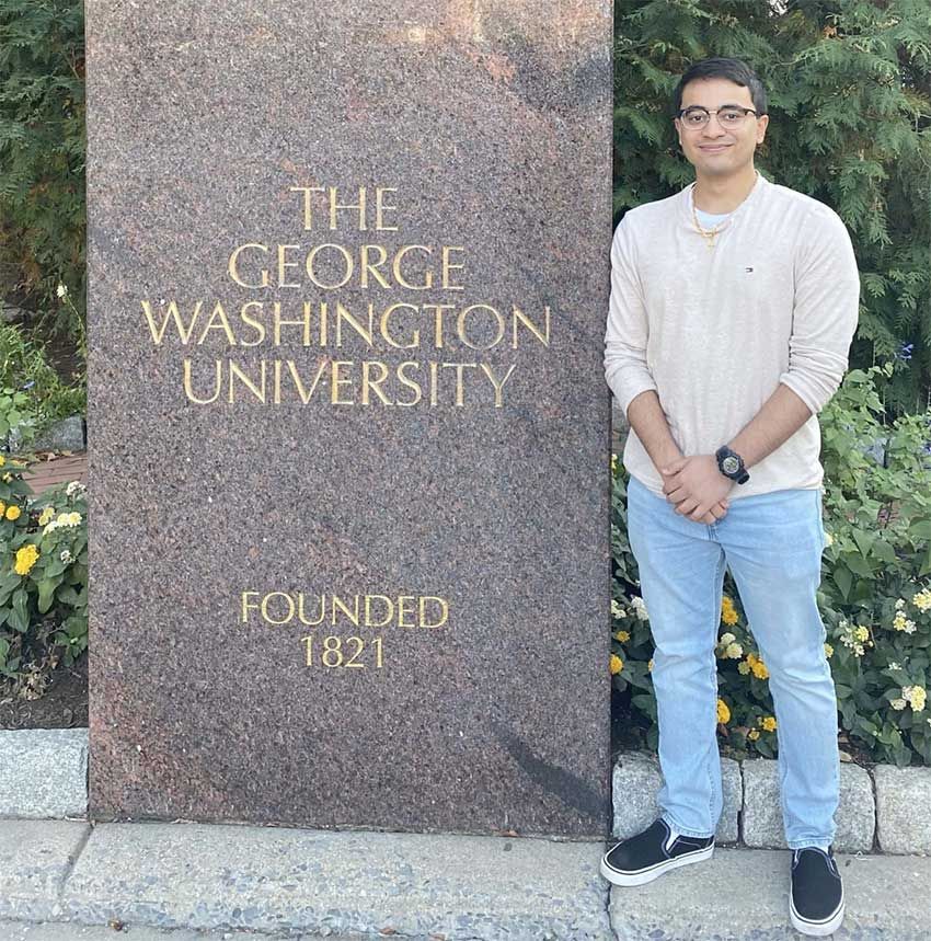 Philip Parel posing for a picture next to the founding date pillar on GW's campus