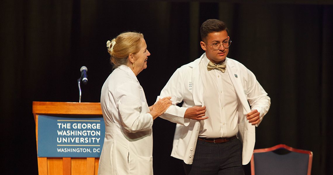 Dean Bass helps student with white coat