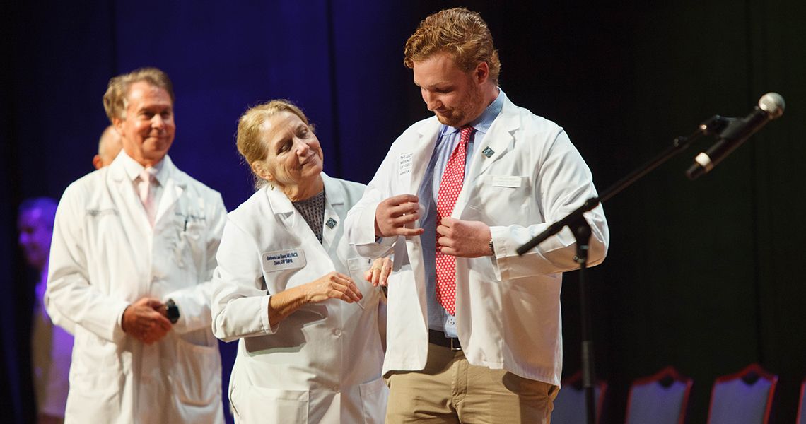 Dean Bass helps student with new white coat