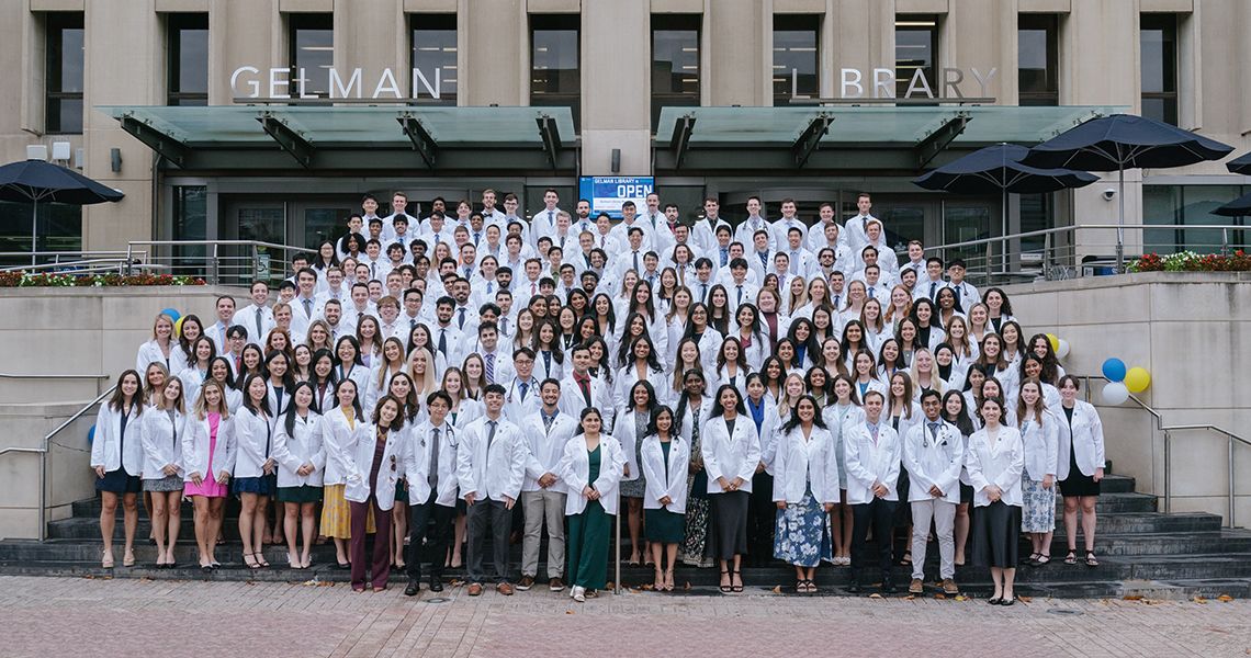 GW MD Class of 2028 in white coats on the steps of Gelman Library