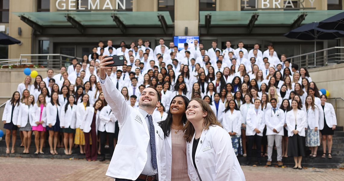 Orientation volunteers pose for selfie in front of Class of 2028 in white coats 