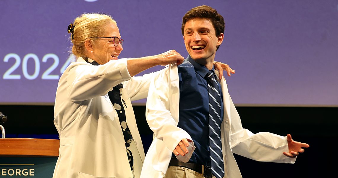 Dean Bass helps med student into his first white coat.