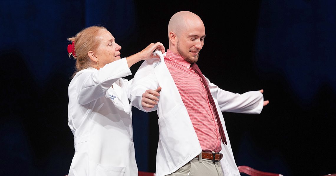 Dean Bass helps a male student put on white coat