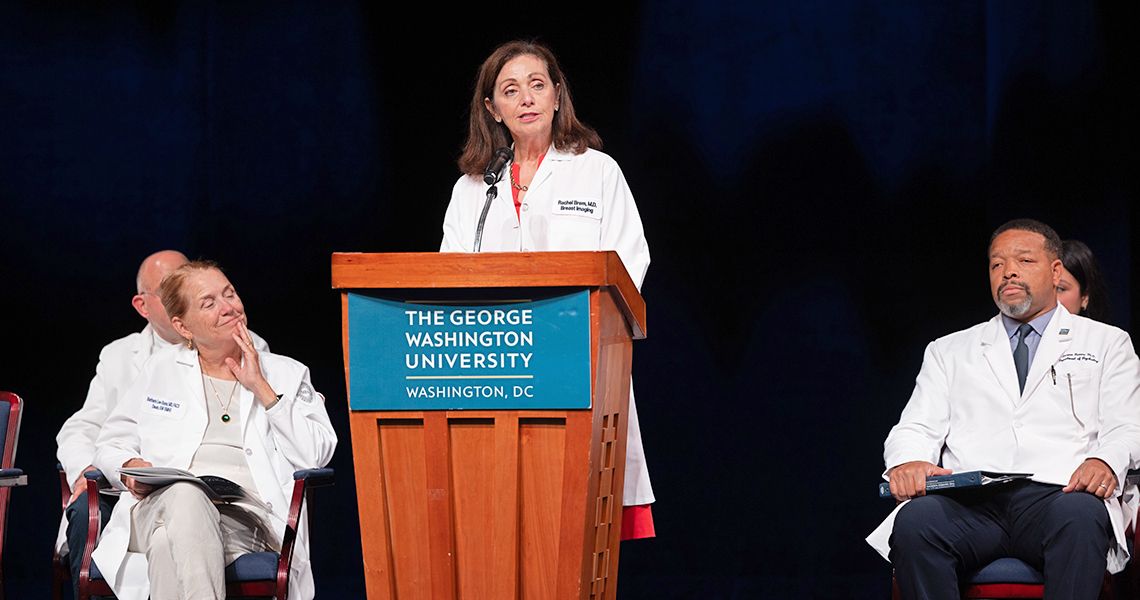 Rachel Brem, MD speaks from podium as Deans Bass (left) and Norris (right) listen 