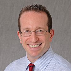 Dr. Adam Friedman smiling and wearing a blue shirt and red tie