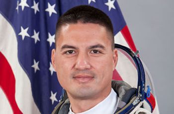 Dr. Kjell Lindgren posing for a portrait in an astronaut suit in front of an American flag