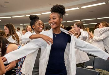 A woman gives another woman a white coat during the PT White Coat Ceremony