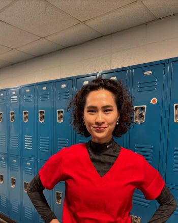 Image of a woman with brown curly hair wearing a black turtleneck and red v-neck t-shirt