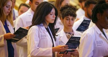 Two students wearing white coats read the White Coat program booklet