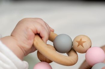 A baby's hand grips a wooden ring and ball chain toy