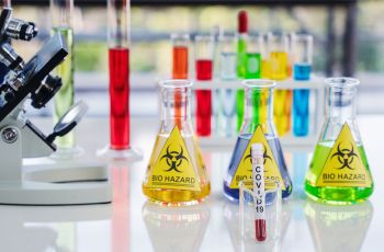 Beakers of multicolored liquid labeled 'biohazard' on a lab table