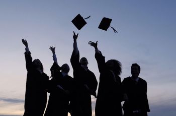 Silhouetted students toss graduation caps into the air