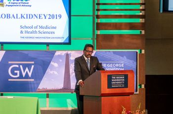 Dr. Dominic Raj speaking from a GW podium on a stage displaying '#GLOBALKIDNEY2019'