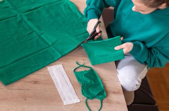 A person cuts green cloth to make a facemask