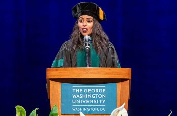 Lillan Dawit in graduation regalia speaking from a podium