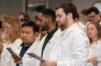 Physician Assistant student wearing white coats recite from a pamphlet