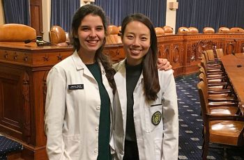 Kristen Schoenike and Garnetta Gonzalez wearing white coats and standing together in a government building