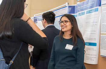 Two medical students speak to each other in front of a presentation poster