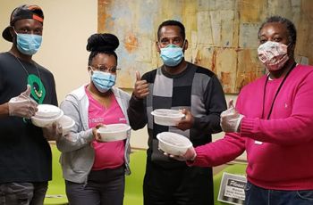 Masked Rodham Insitute staff hold meal containers and give thumbs-up