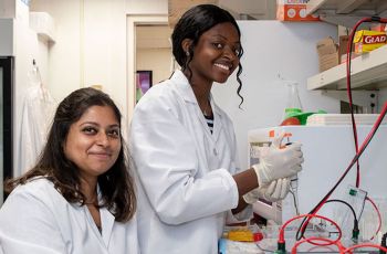 Two students in the GW summer program wearing white coats and working in a lab
