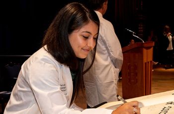 A GW MD student in a white coat signs a ceremonial oath
