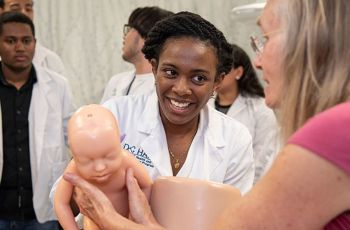 A highschooler smiling at a GW doctor giving a demonstration with a mannequin baby