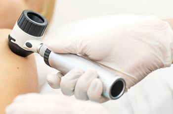 A gloved hand holds a skin examining tool against a patient's shoulder