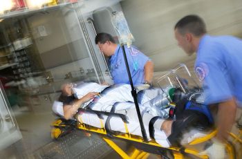 Two EMTs pushing a person on a stretcher into an ambulance