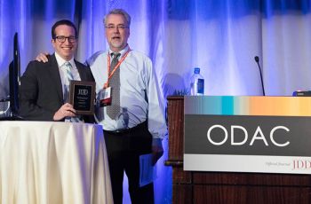 Dr. Adam Friedman holding an award on stage with a man next to a podium that reads 'ODAC'