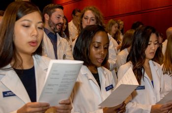 Members of the PA Class of 2019 wearing short white coats and reciting from a pamphlet