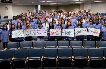 SMHS students stand together in an auditorium holding signs that spell out 'We are SMHS scrubs addressing the firearm epidemic'