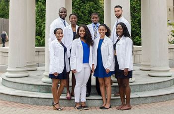 Eight GW medical students standing together in white coats in front of a rotunda