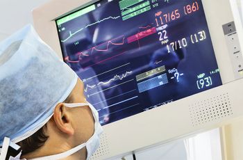 A medical professioal wearing a cap and mask looking at a display monitor