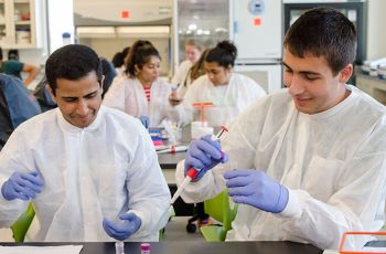 Two high school students wearing white coats and gloves participating in a medical laboratory sciences summer immersion program