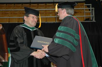 James Finkelstein in graduation regalia shaking hands with a SMHS faculty member