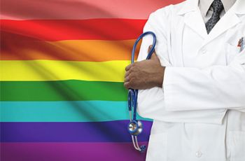 A doctor seen from the neck-down holding a stethoscope in front of a LGBTQI flag