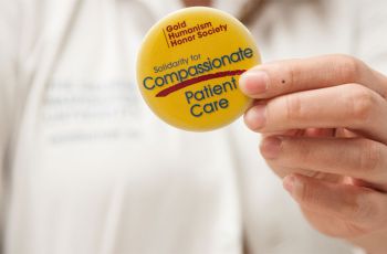 Person holding a golden pin with text on it | Gold Humanism Honor Society Solidarity for Compassionate Patient Care