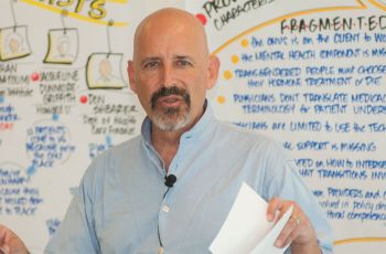Robert Mittman holding paper and standing in front of a whiteboard