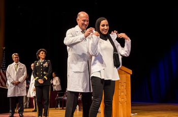 Dean Jeffrey Akman putting a white coat on a medical student