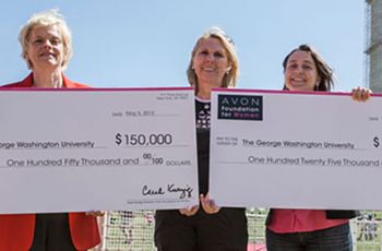 Patricia Berg and Mandi Pratt-Chapman holding large checks from the Avon Foundation and standing outdoors
