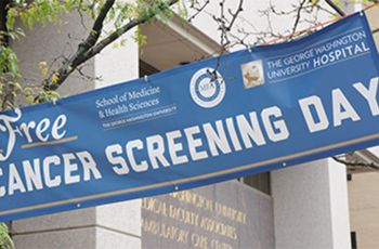 "Free Cancer Screening Day" | Blue Banner hanging between trees outdoors