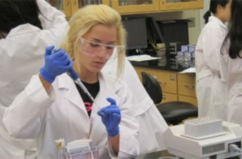 Woman in white lab coat and blue gloves using a pipette