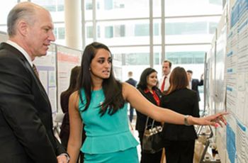 A medical student showing her research poster to SMHS Dean Jeffrey Akman