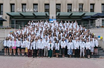 Class of 2028 poses in white coats on steps of Gelman Library