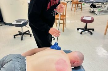 Student uses plunger for soft tissue mobilization during Manual Therapy Club