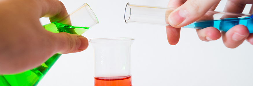 Someone pouring different colored liquids into a beaker